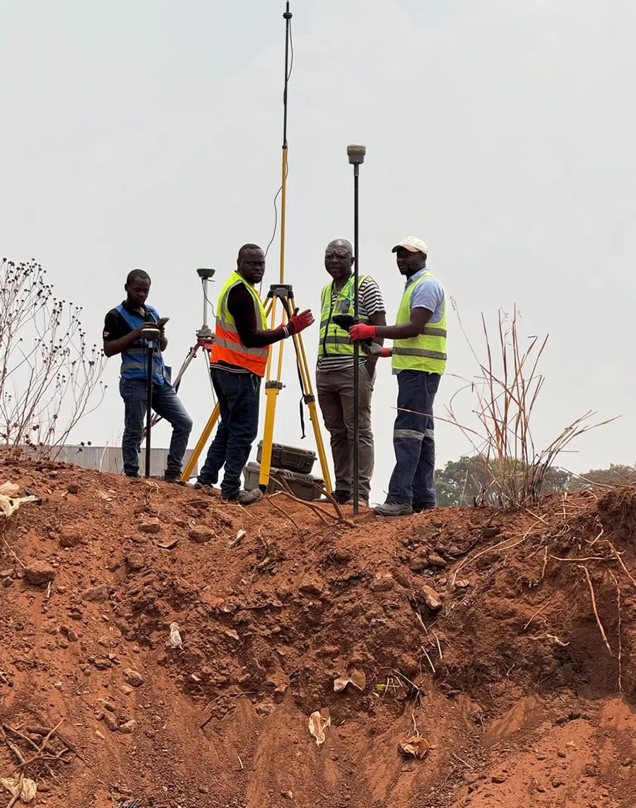 A team of four surveyors from Horizon Engineering and Services, wearing high-visibility vests, use GNSS receivers and tripods atop a large mound of red earth at a construction site in Kolwezi, DR Congo.